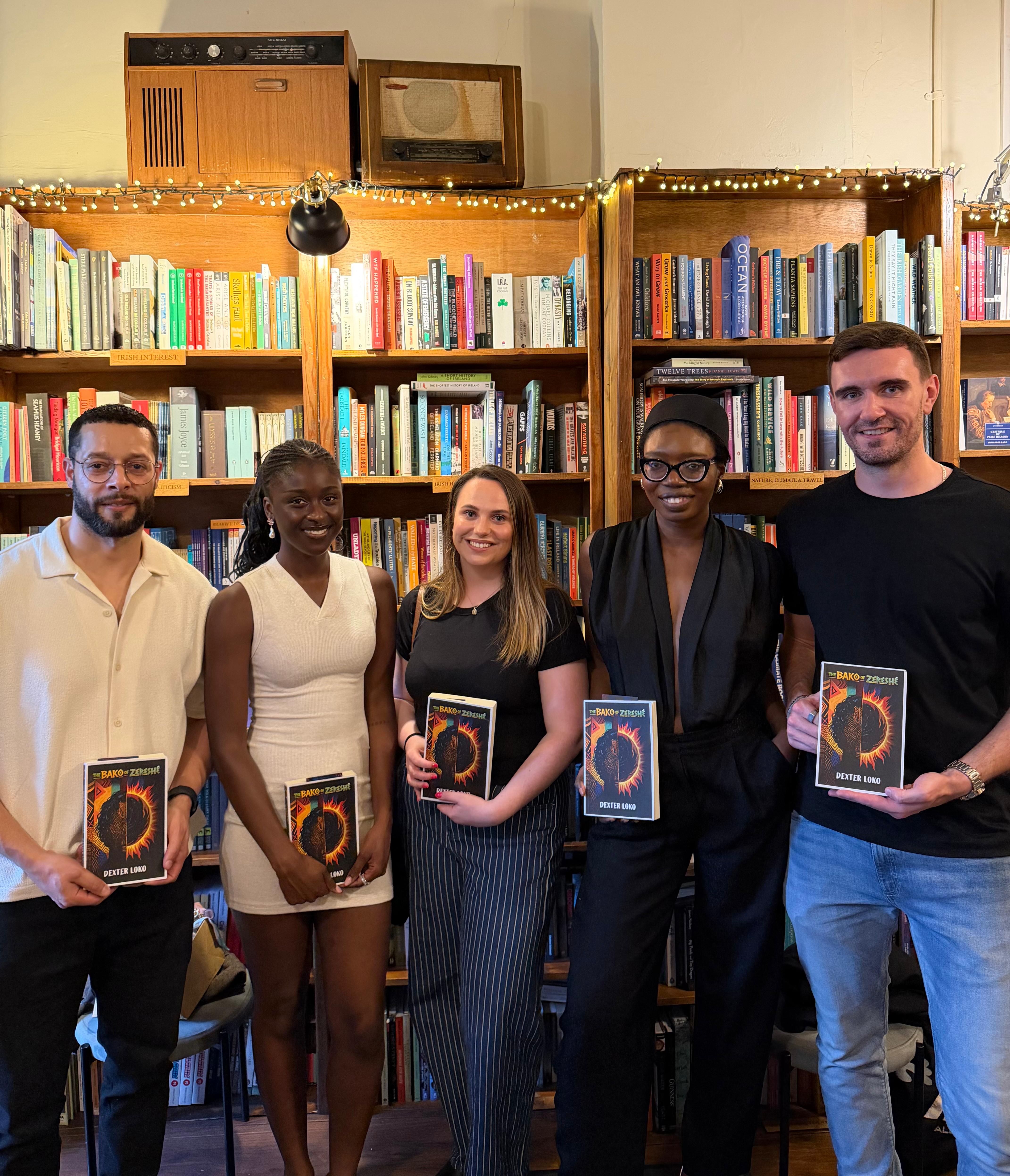 Five people holding copies of The Bako of Zereshé in a book-filled room.